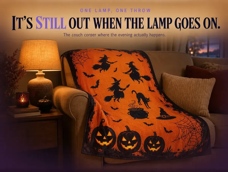 A couch corner in the evening with a single lamp lit and the witch-print throw draped over the arm.