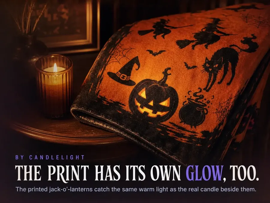 A folded corner of the throw beside a single lit candle, warm light catching the printed jack-o'-lanterns.
