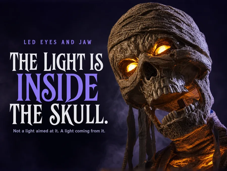 Night macro of the mummy's wrapped skull face, both eye sockets glowing amber-orange.