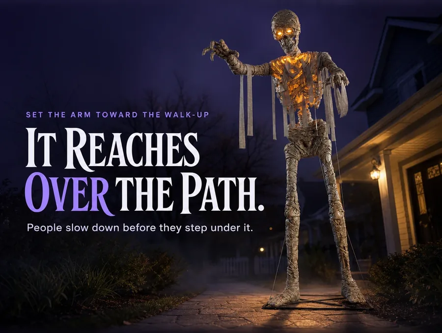 The mummy beside a front walkway at dusk, one arm reaching over the path, glow starting to show.